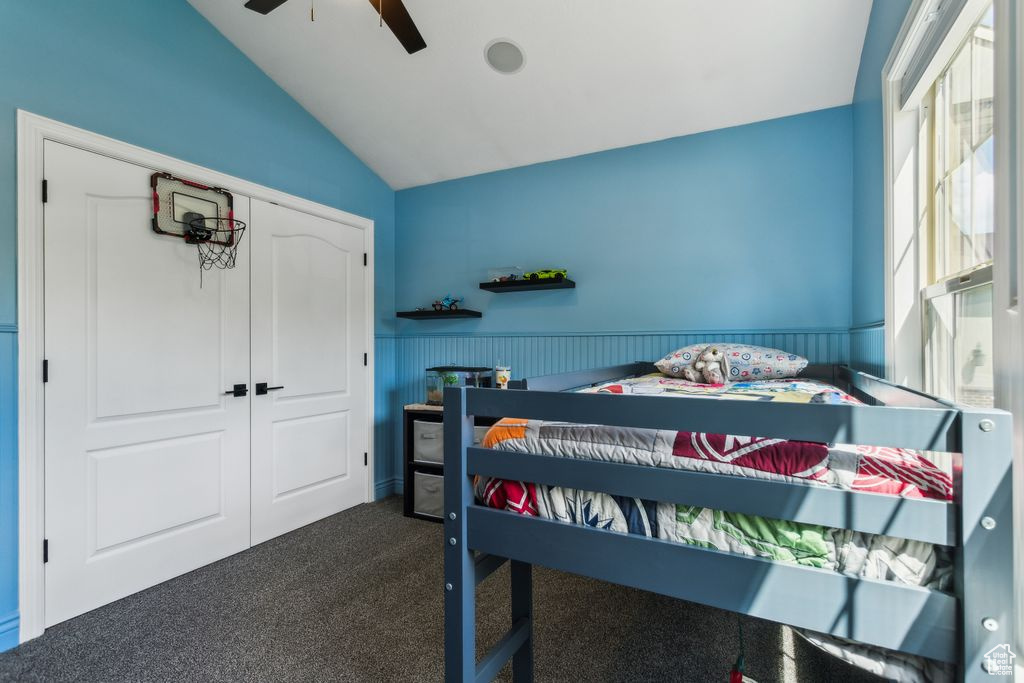 Bedroom with lofted ceiling, dark colored carpet, wainscoting, a ceiling fan, and a closet