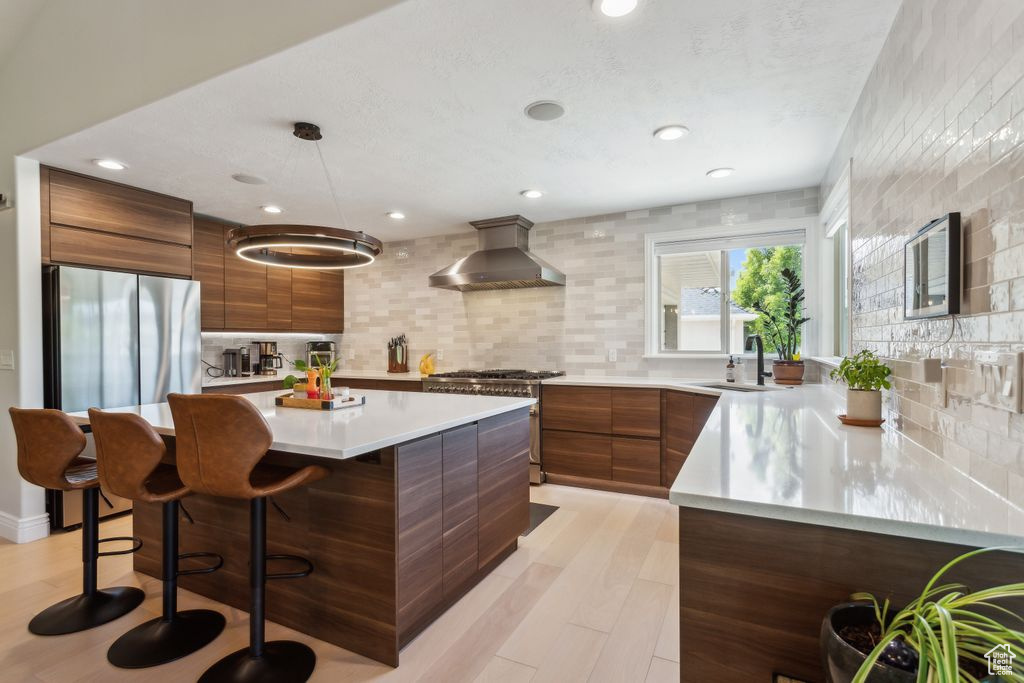 Kitchen featuring wall chimney exhaust hood, appliances with stainless steel finishes, modern cabinets, tasteful backsplash, and recessed lighting