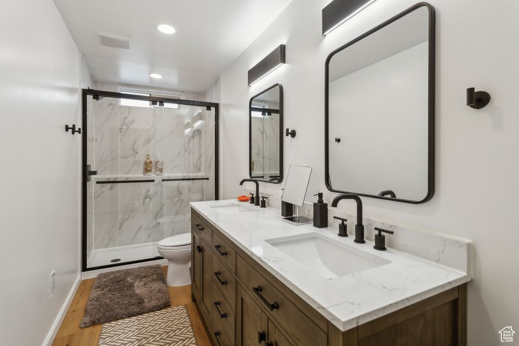 Bathroom featuring double vanity, a marble finish shower, wood finished floors, and recessed lighting