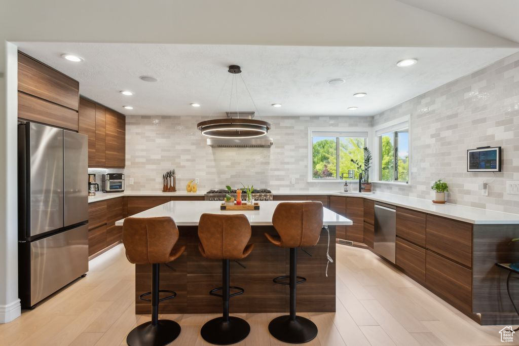 Kitchen with appliances with stainless steel finishes, modern cabinets, brown cabinetry, backsplash, and a breakfast bar