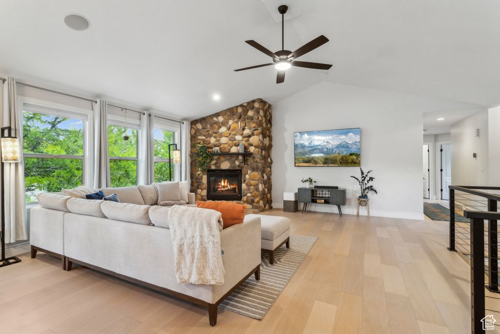 Living area with a ceiling fan, light wood-style flooring, vaulted ceiling, and a fireplace
