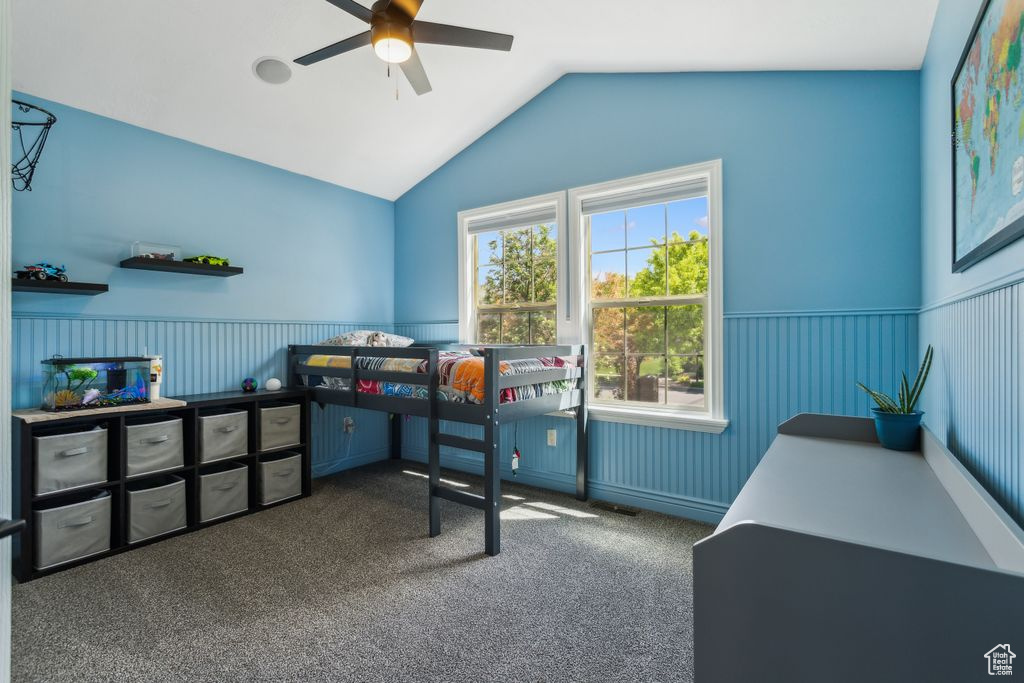 Bedroom with vaulted ceiling, a wainscoted wall, carpet flooring, and ceiling fan