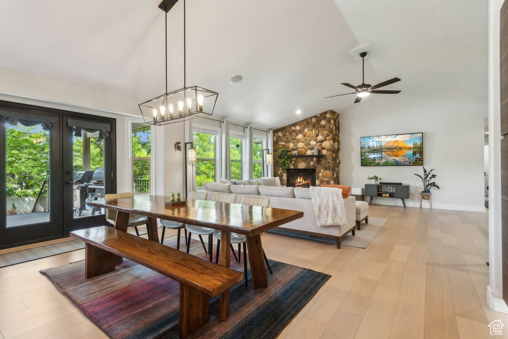 Dining room with lofted ceiling, a stone fireplace, ceiling fan, light wood-style flooring, and french doors