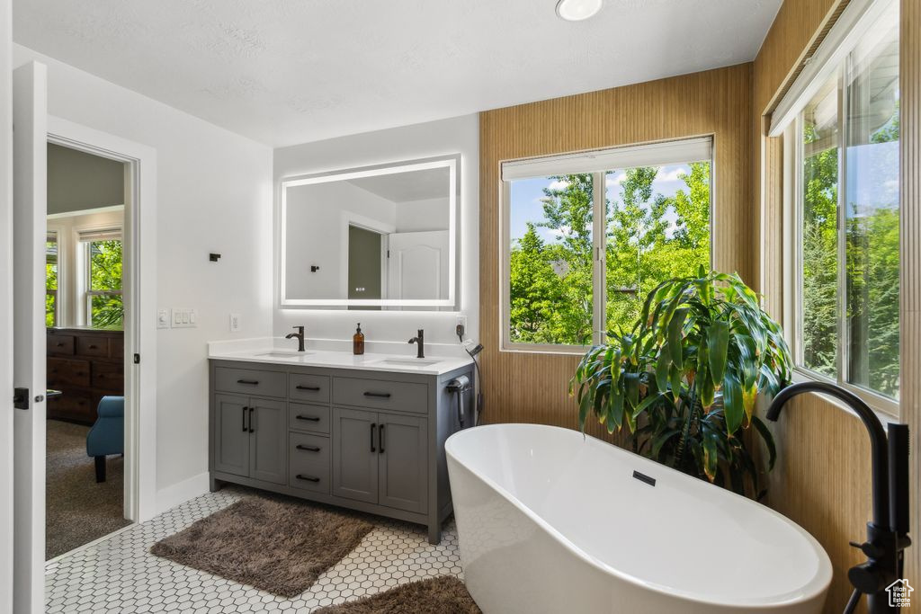 Full bath featuring a freestanding bath, double vanity, plenty of natural light, and wood walls