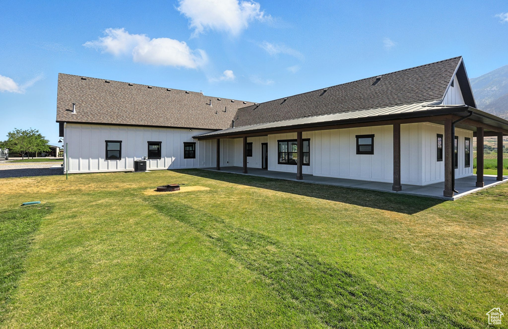 Rear view of property featuring a lawn, a patio area, a metal roof, board and batten siding, and a shingled roof
