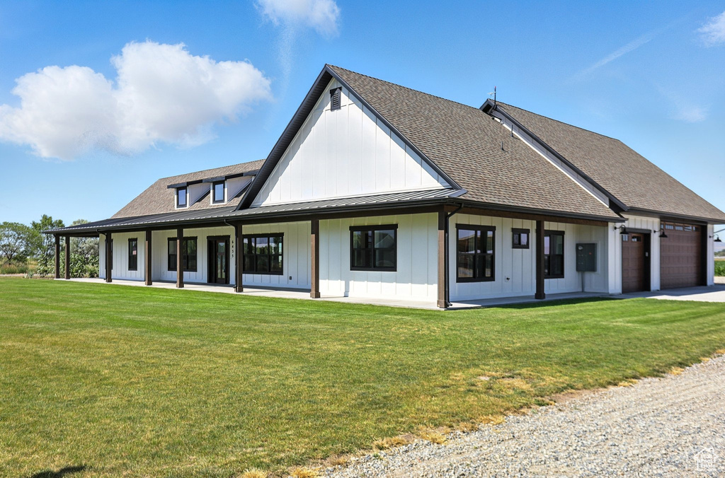 Back of house featuring board and batten siding, a garage, roof with shingles, a lawn, and driveway