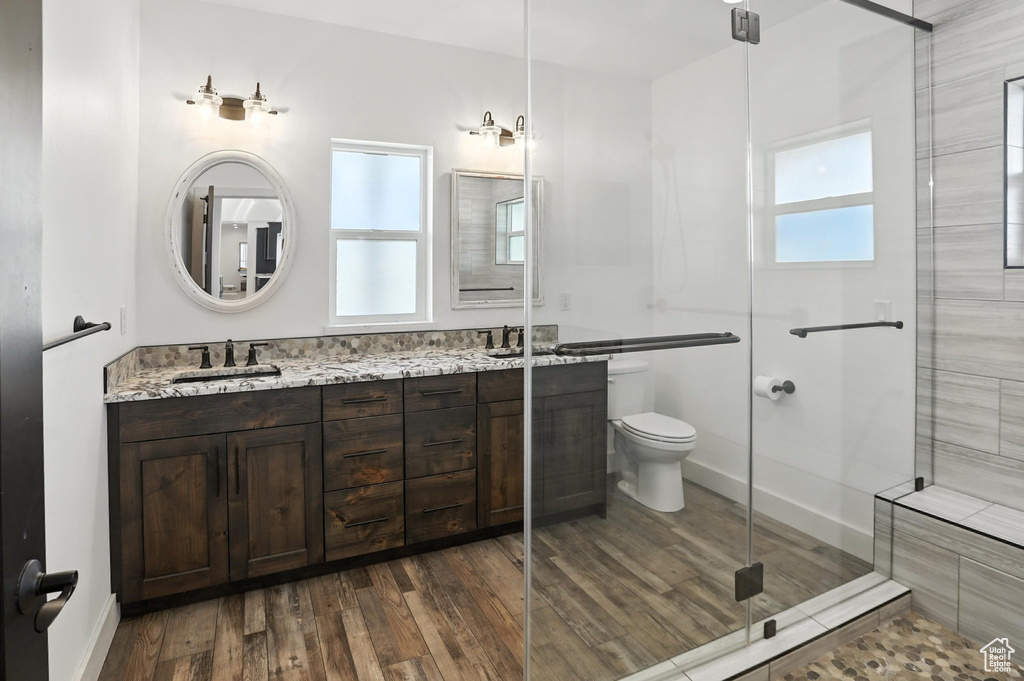 Full bathroom featuring healthy amount of natural light, double vanity, wood finished floors, and a shower stall