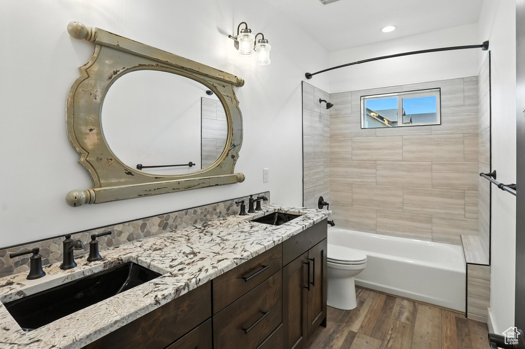 Bathroom with double vanity, shower / bath combination, wood finished floors, and recessed lighting