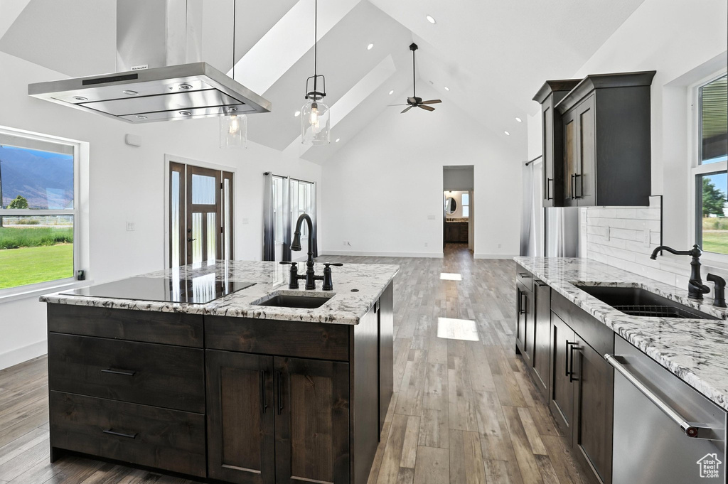 Kitchen with stainless steel dishwasher, exhaust hood, high vaulted ceiling, light wood-type flooring, and light stone counters