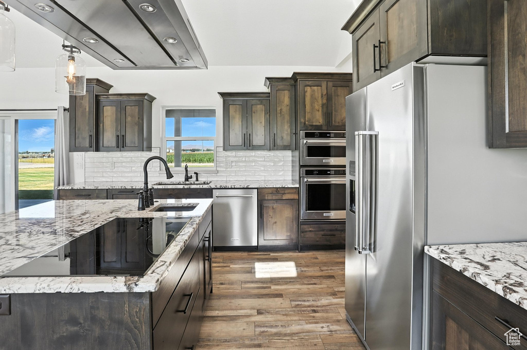 Kitchen with stainless steel appliances, dark wood finished floors, dark brown cabinets, light stone counters, and tasteful backsplash