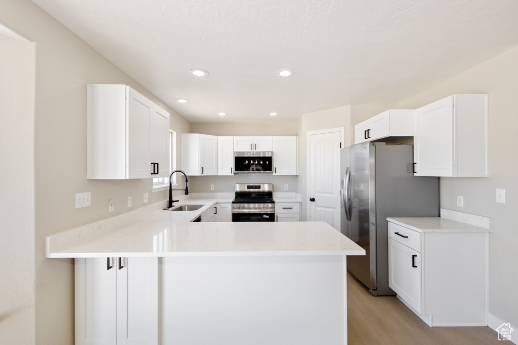 Kitchen with stainless steel appliances, light wood-style flooring, a peninsula, light countertops, and white cabinetry