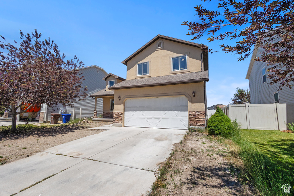 Traditional-style home with stucco siding, stone siding, a garage, and concrete driveway