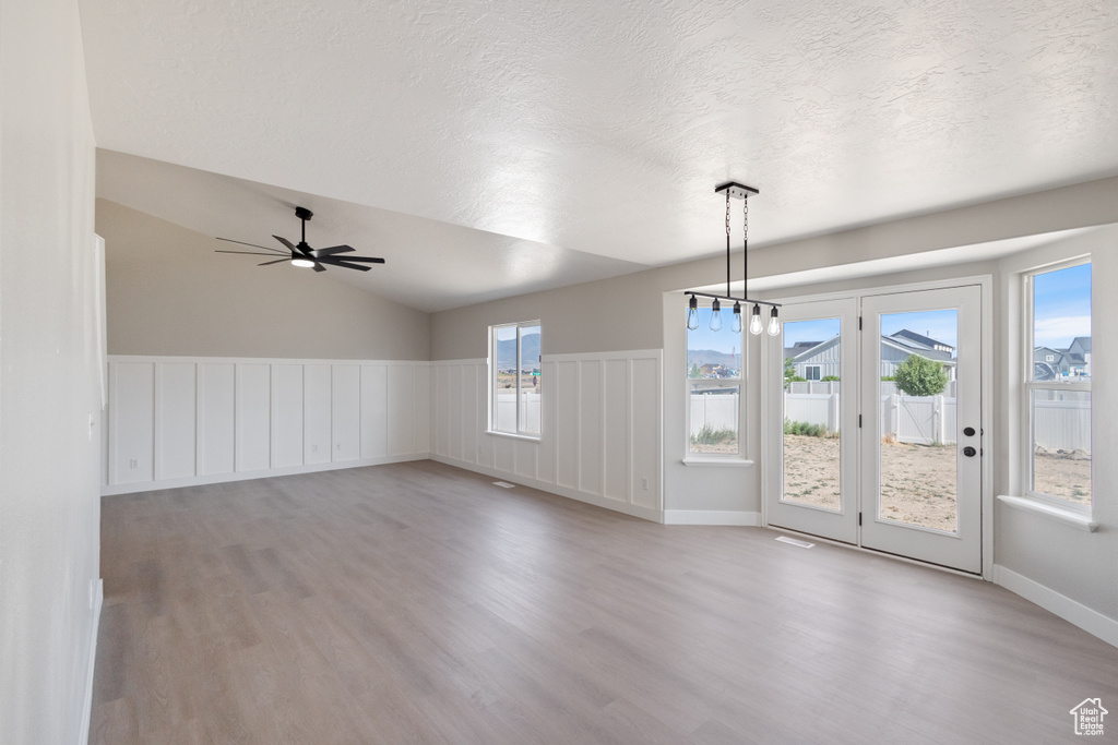 Unfurnished room featuring light wood-style floors, ceiling fan, a textured ceiling, vaulted ceiling, and a wainscoted wall