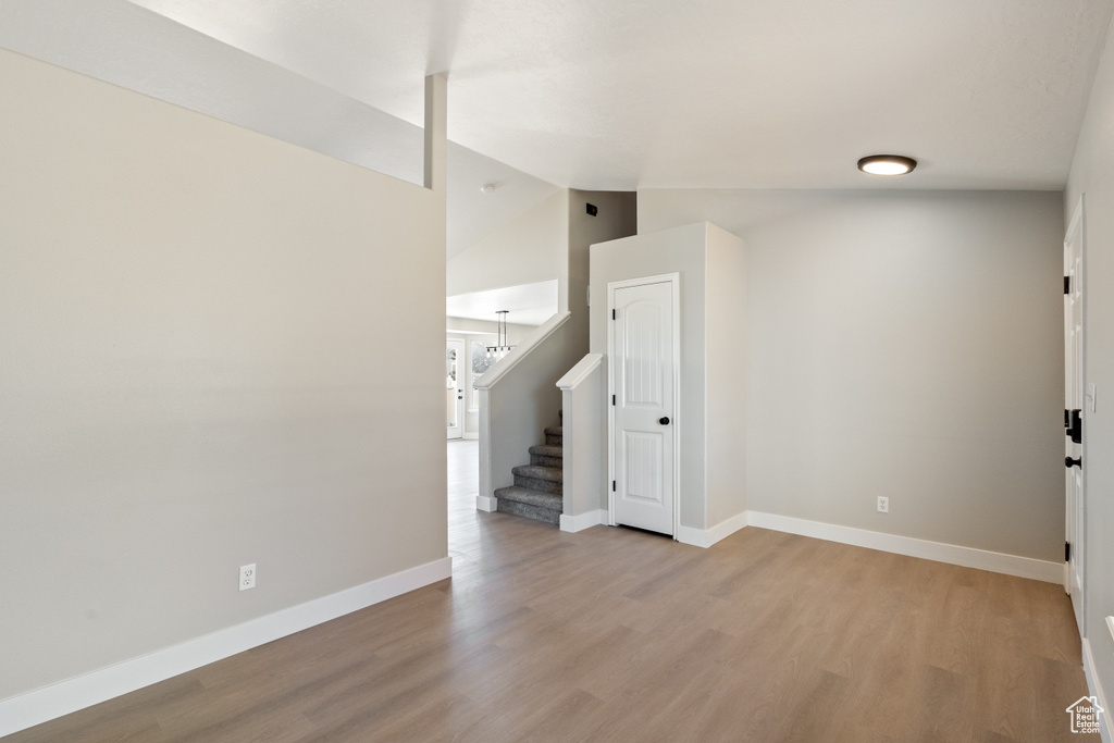 Unfurnished room with light wood-type flooring, stairway, and lofted ceiling
