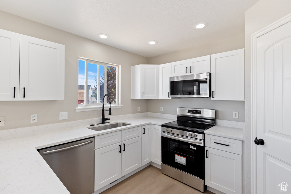 Kitchen featuring stainless steel appliances, white cabinets, recessed lighting, light countertops, and light wood-style flooring