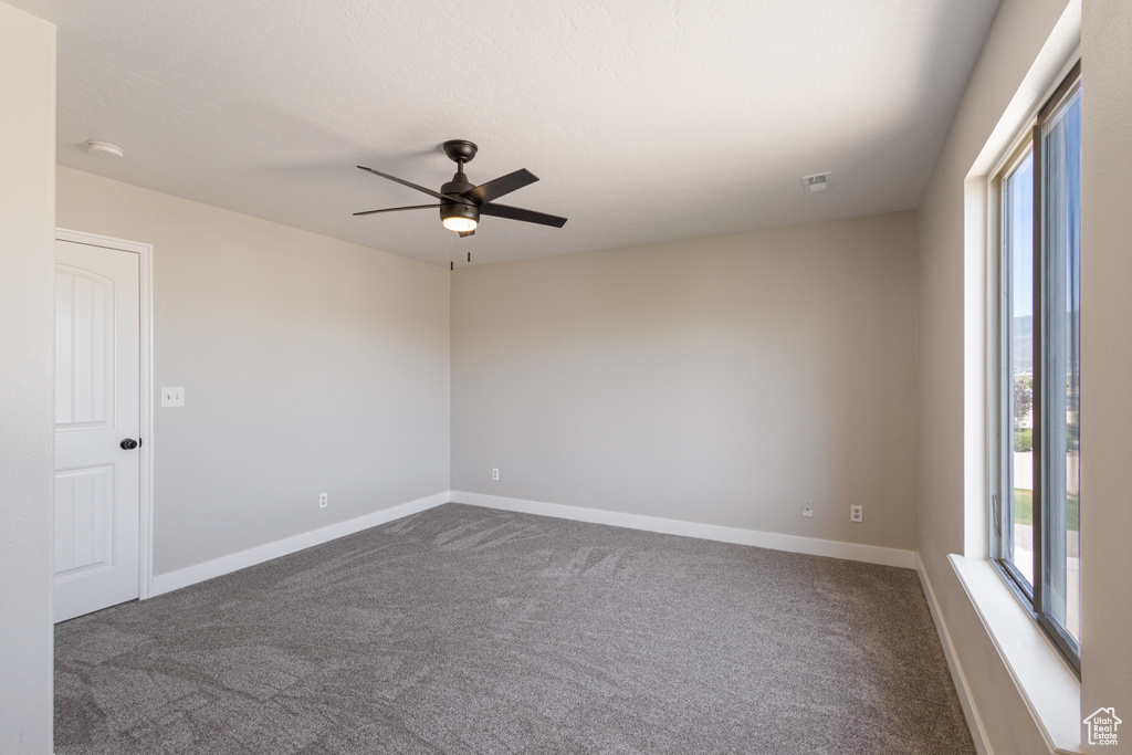 Empty room with dark carpet, ceiling fan, and a smoke detector