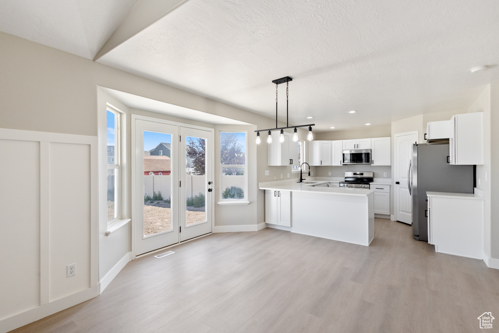 Kitchen with stainless steel appliances, a peninsula, light wood-style flooring, white cabinetry, and recessed lighting