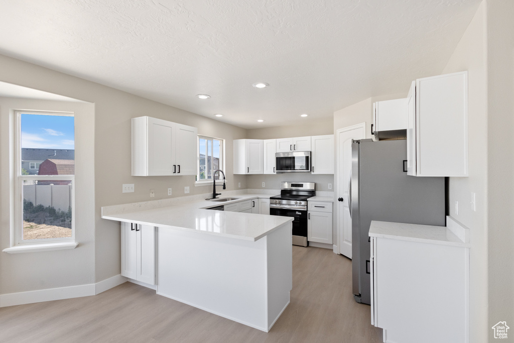 Kitchen with stainless steel appliances, light wood-style floors, a peninsula, light countertops, and recessed lighting