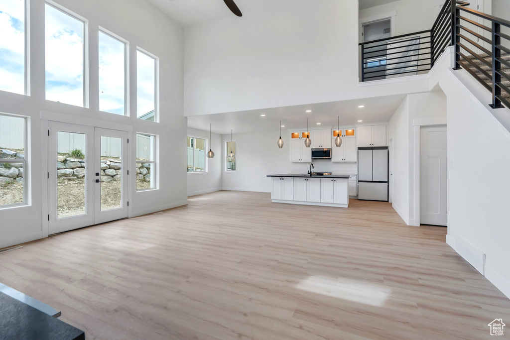 Unfurnished living room with a towering ceiling, healthy amount of natural light, light wood-style floors, and recessed lighting