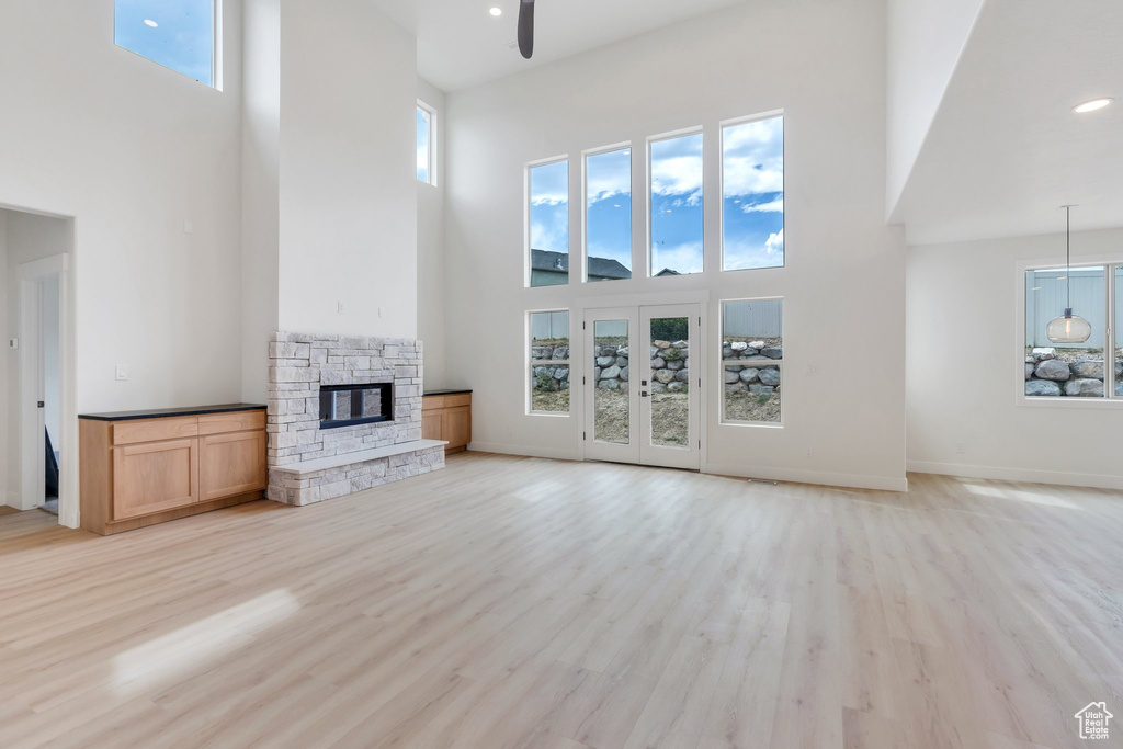 Unfurnished living room with a high ceiling, a ceiling fan, a fireplace, light wood-style flooring, and recessed lighting