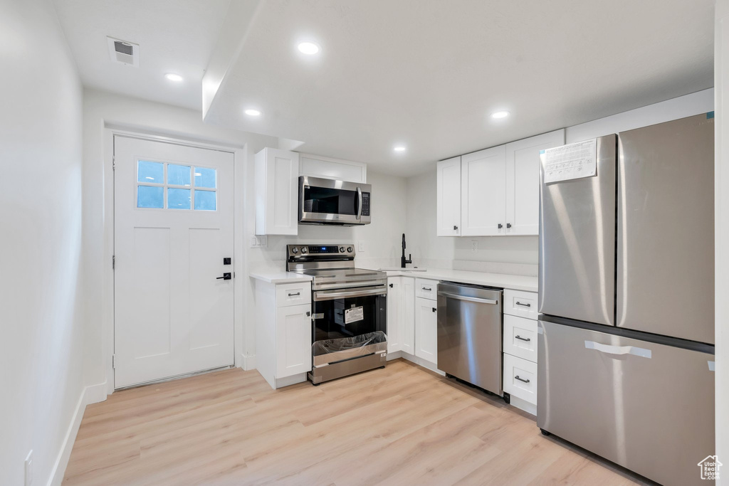Kitchen featuring appliances with stainless steel finishes, light wood-type flooring, light countertops, white cabinets, and recessed lighting