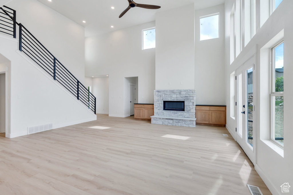 Unfurnished living room with a high ceiling, a fireplace, light wood-style floors, ceiling fan, and recessed lighting