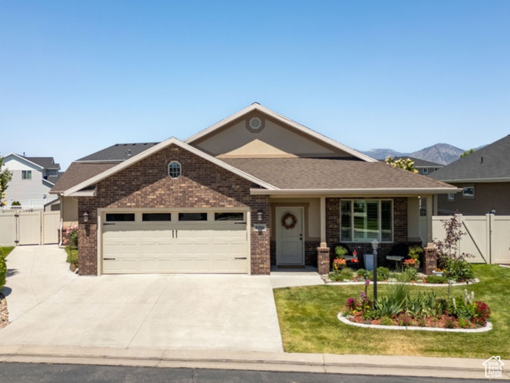 View of front facade with concrete driveway, brick siding, an attached garage, a gate, and a shingled roof
