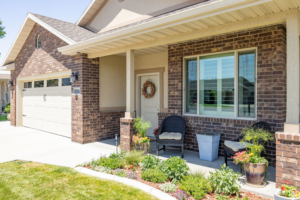 Property entrance featuring brick siding, a garage, a porch, concrete driveway, and roof with shingles