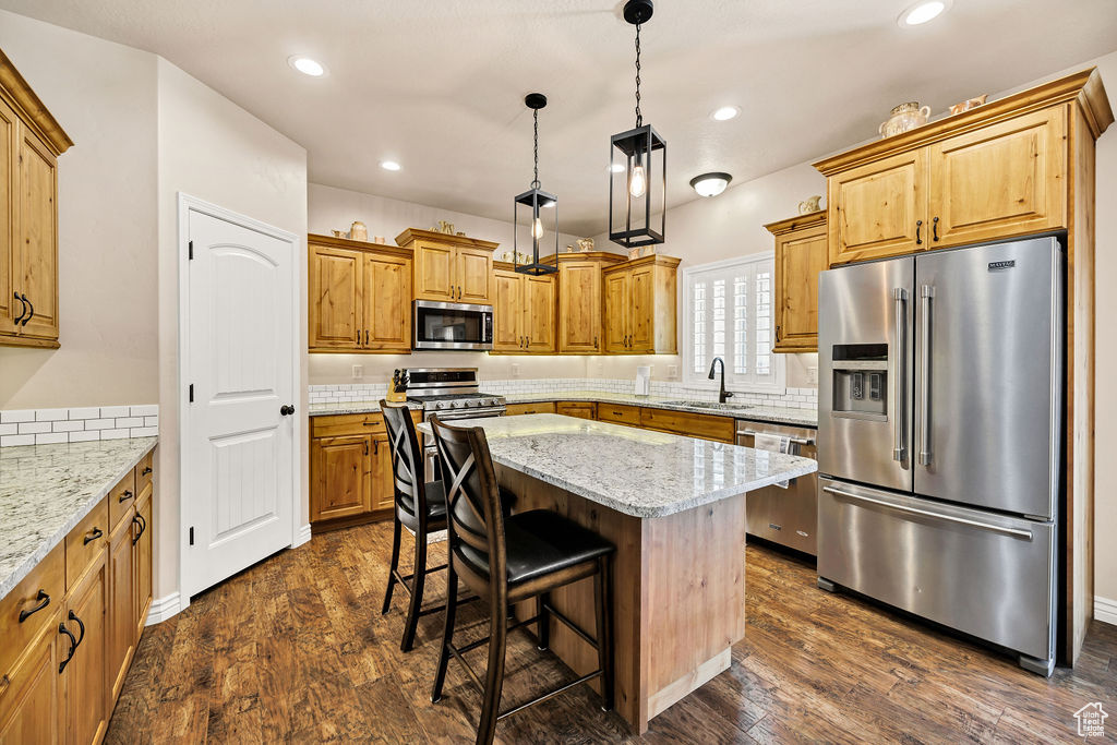 Kitchen featuring stainless steel appliances, a center island, dark wood-style floors, light stone counters, and a breakfast bar