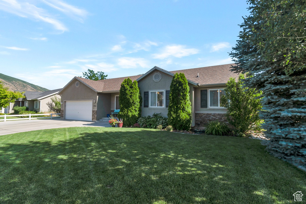 Ranch-style home with concrete driveway, stone siding, a front yard, stucco siding, and a garage