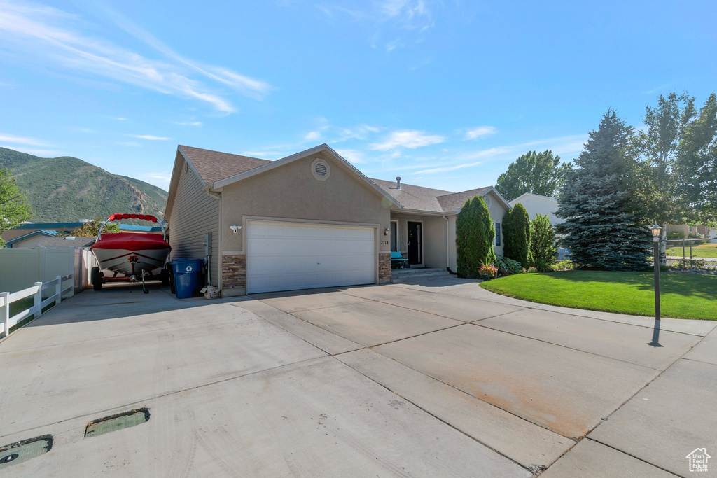 Ranch-style house with an attached garage, driveway, a mountain view, stone siding, and stucco siding