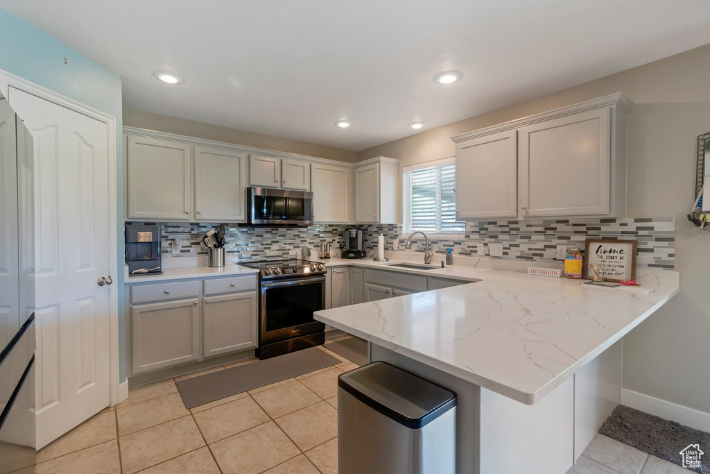 Kitchen featuring appliances with stainless steel finishes, a peninsula, decorative backsplash, light tile patterned floors, and light stone countertops