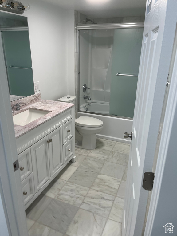 Bathroom featuring marble look tiles, vanity, and bath / shower combo with glass door