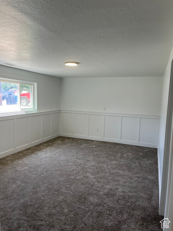 Carpeted spare room featuring a decorative wall, a textured ceiling, and a wainscoted wall