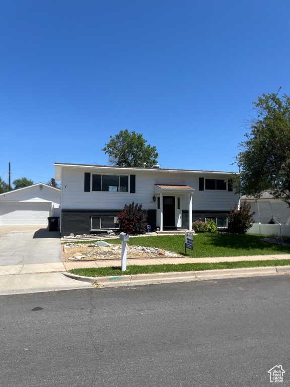 Split foyer home with concrete driveway, an outdoor structure, and a front lawn