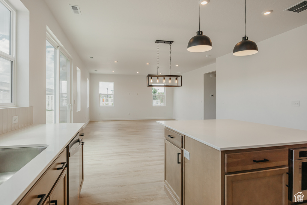 Kitchen with light wood finished floors, stainless steel dishwasher, hanging light fixtures, light countertops, and recessed lighting