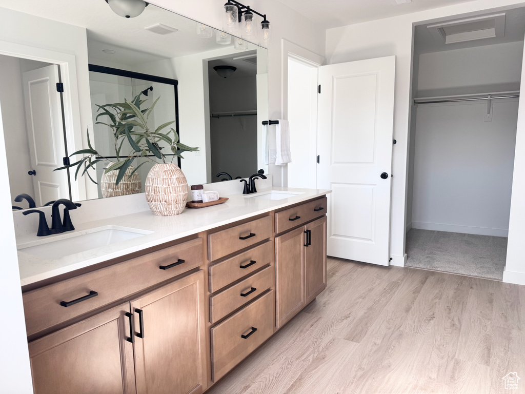 Full bath with a walk in closet, double vanity, wood finished floors, and an enclosed shower