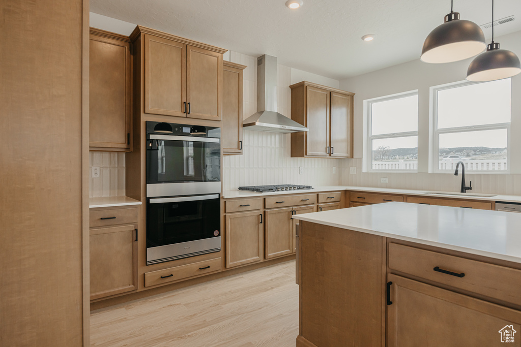 Kitchen featuring stainless steel appliances, wall chimney range hood, light wood-type flooring, decorative backsplash, and recessed lighting