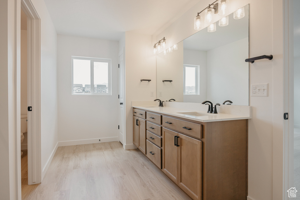 Full bath with double vanity, healthy amount of natural light, and wood finished floors