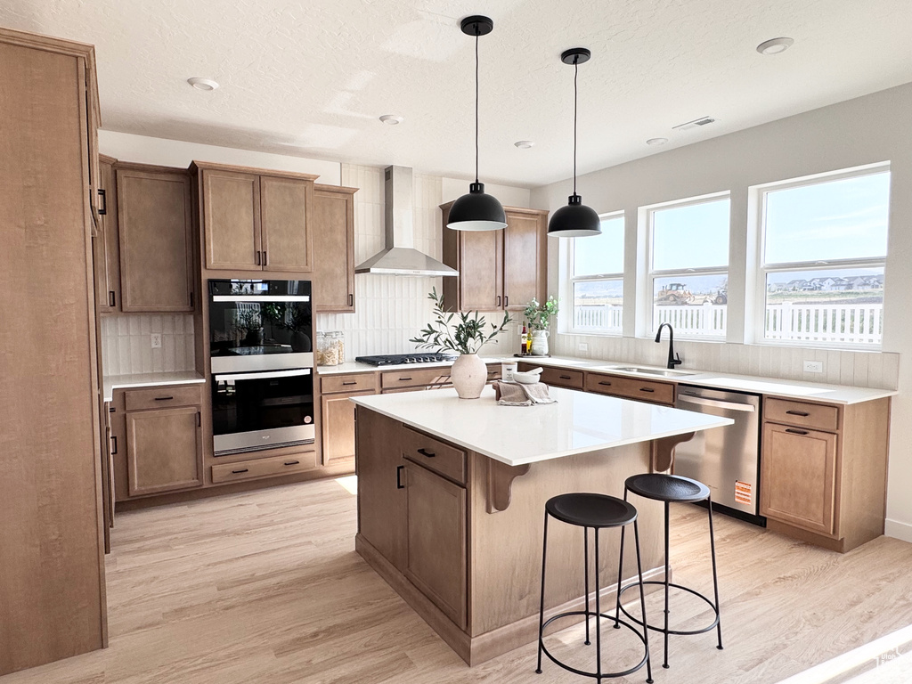Kitchen featuring wall chimney exhaust hood, appliances with stainless steel finishes, decorative backsplash, light wood-type flooring, and recessed lighting