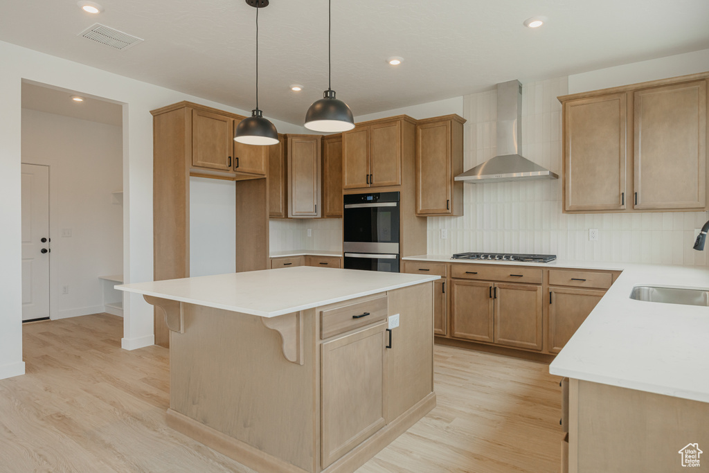 Kitchen with wall chimney range hood, double wall oven, light wood-style flooring, a center island, and recessed lighting