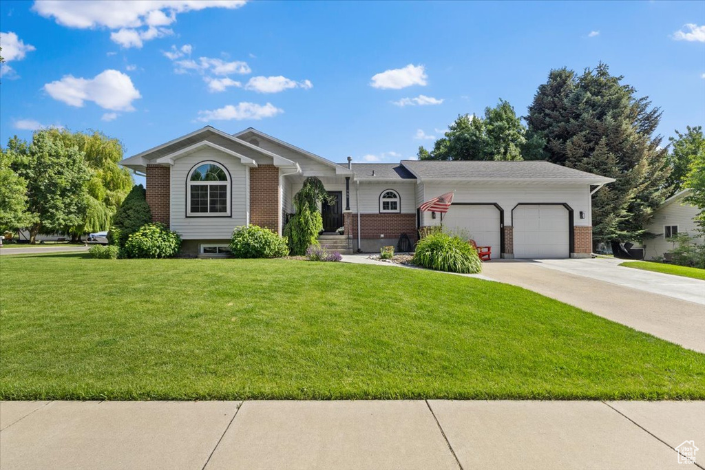 View of front of home featuring an attached garage, brick siding, a front lawn, and driveway