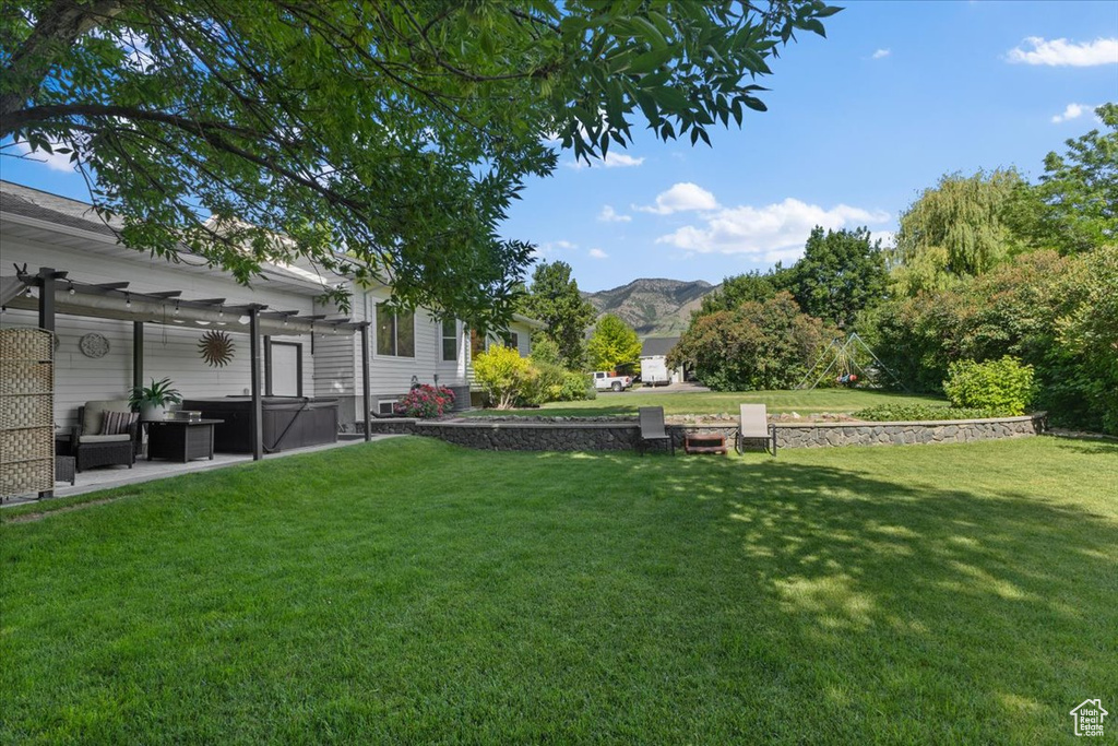 View of green lawn with a hot tub, a pergola, a mountain view, and a patio area