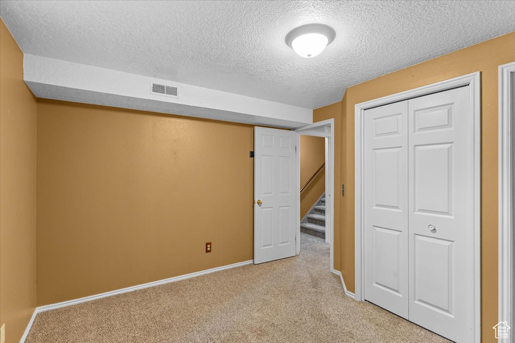 Unfurnished bedroom featuring light colored carpet, a textured ceiling, and a closet