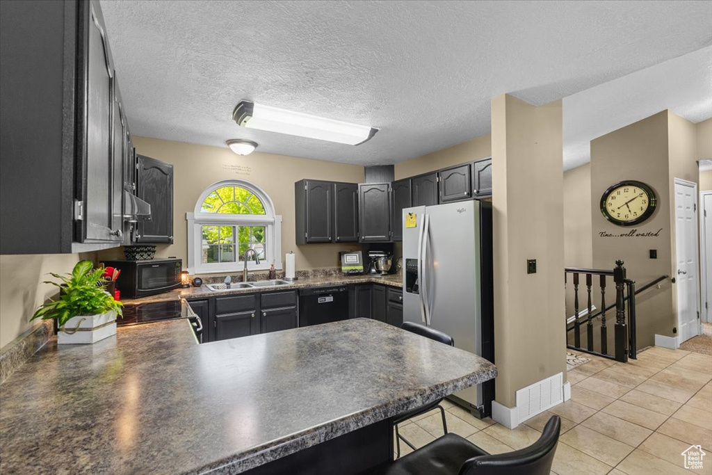 Kitchen with a peninsula, black appliances, dark countertops, light tile patterned floors, and a kitchen breakfast bar