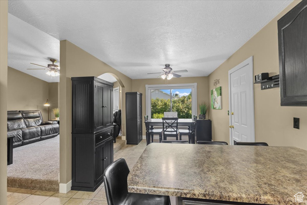 Kitchen featuring ceiling fan, light tile patterned flooring, dark cabinetry, and a textured ceiling
