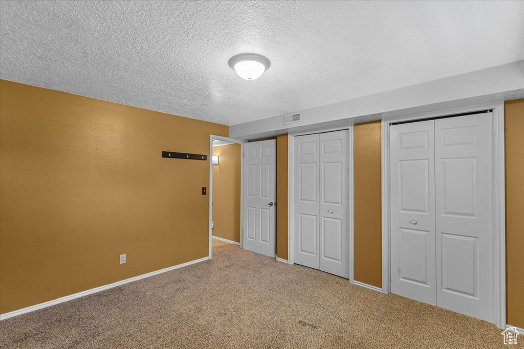 Unfurnished bedroom featuring a textured ceiling, carpet, and two closets