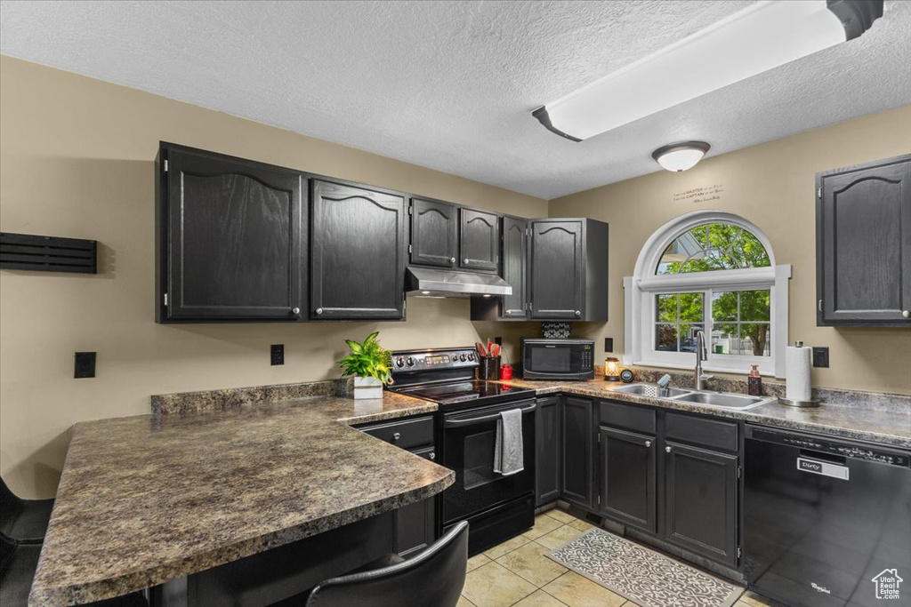 Kitchen featuring black appliances, under cabinet range hood, dark countertops, a peninsula, and a textured ceiling