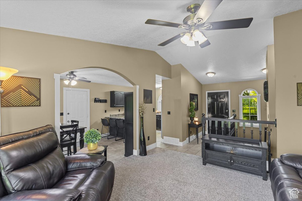 Living area with a ceiling fan, arched walkways, vaulted ceiling, light colored carpet, and light tile patterned flooring