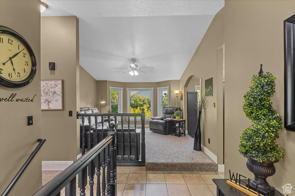 Hallway featuring an upstairs landing, a textured ceiling, carpet flooring, arched walkways, and tile patterned floors